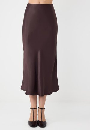Midilanger, dunkelbrauner Satinrock, kombiniert mit schwarzen T-Riemchen-Absätzen, gezeigt von der Taille bis zu den Füßen vor einem einfarbigen Hintergrund.