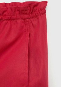 Rdeče jogger hlače z elastičnim pasom, gladko teksturo in stransko žepno podrobnostjo. Material deluje lahko in zračno.