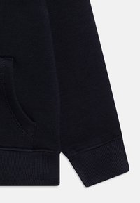 Dettaglio di una felpa blu navy scuro con polsini a coste, tasca frontale e tessuto testurizzato. Presenta cuciture dritte e una finitura liscia.