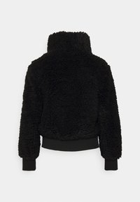 Czarna kurtka z futra sztucznego z wysokim kołnierzem, teksturowaną powierzchnią, ściągaczami przy rękawach i u podstawy. Posiada krótki krój i luźny fason.