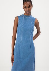 Vestido de mezclilla sin mangas en azul claro, con cuello alto, corte entallado y costuras verticales para dar forma. Textura suave y líneas limpias.