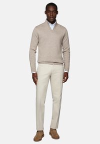Beige knit sweater with a V-neck, paired with cream trousers and brown suede ankle boots. Smooth texture, fitted design, and subtle details.