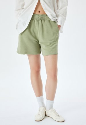Gröna shorts i bomullsblandning med elastisk midja, sidofickor och avslappnad passform, tillsammans med vita sneakers och ankelsockor.
