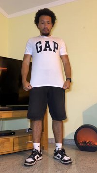 White t-shirt with a black “GAP” logo, paired with dark denim shorts and black and white sneakers, standing on a tiled floor.