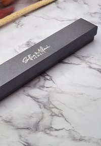 Scatola di gioielli nera con texture e logo metallico "Sofia Milani Jewels", forma rettangolare, posata su una superficie di marmo.