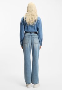 Camisa vaquera azul claro y jeans de corte ancho, con un degradado que se desvanece, dos bolsillos traseros y una etiqueta negra en la cintura.