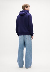 Marineblå hettegenser med snøre og kengurulomme, kombinert med lyseblå vide jeans med baklommer og råkant.