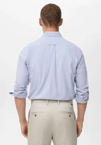 Hellblau gestreiftes Hemd mit hochgerollten Ärmeln, Rückenfalte und kontrastierenden cremefarbenen Hosen. Glattes Material, taillierte Passform, dezentes Design.