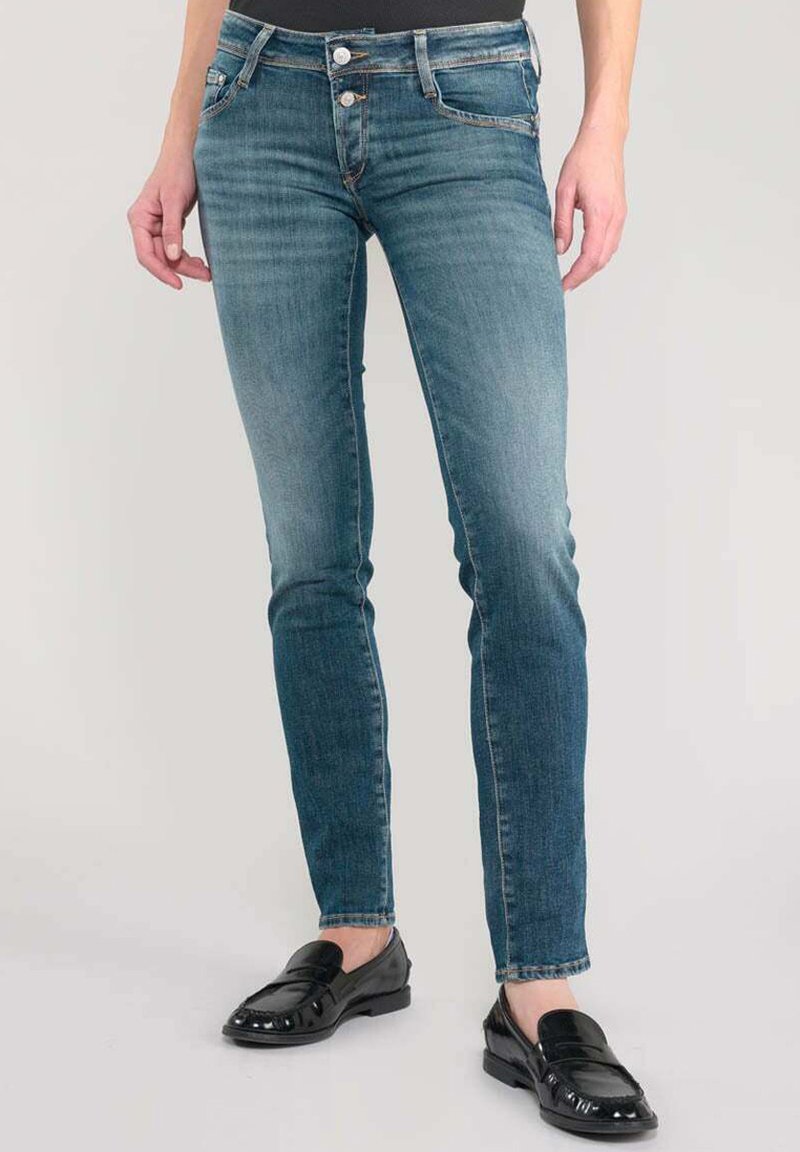 Jeans skinny en denim bleu délavé, avec un design à cinq poches, une fermeture à bouton et un léger effet usé. Portés avec des mocassins noirs.