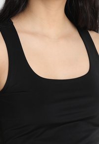 Czarna bluzka na ramiączkach z szerokim, okrągłym dekoltem i wąskimi ramiączkami, wykonana z gładkiego, elastycznego materiału. Prosty, bezszwowy fason.