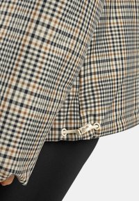 Tessuto a righe in beige, blu navy e marrone, con un gancio e un cordino all'orlo per la regolazione. Superficie liscia e testurizzata con una vestibilità su misura.