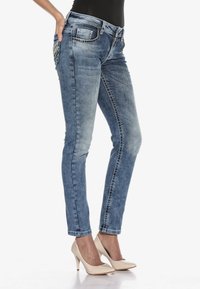 Eng gefittete blaue Jeans mit ausgeblichenem Wasch-Effekt, fünf Taschen und dekorativer Stickerei, kombiniert mit beigen High-Heels.