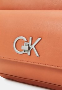 Oranžová kožená kabelka s stříbrným logem "CK" s uzamykacím mechanismem, detailním prošíváním a hladkou texturou.