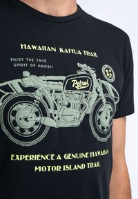 Černé tričko s potiskem zeleného motocyklu a textem: "Hawaiian Kanu Trail" a "Petrol Ind." Měkká tkanina, kulatý výstřih, volný střih.