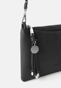 Bolso de cuero negro con cierre de cremallera, equipado con una correa de cadena, herrajes metálicos y flecos decorativos con detalles en plata.