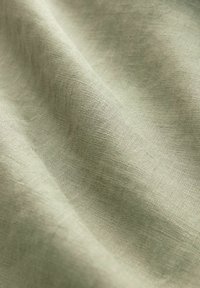 Tissu tissé beige clair avec des plis doux mettant en valeur la texture et les détails fins de la surface du matériau.