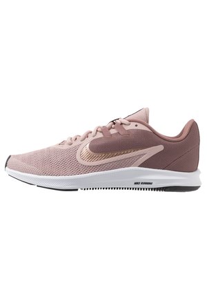 Chaussure de course Nike rose clair avec dessus en mesh, semelle blanche et logo Swoosh métallique sur le côté.