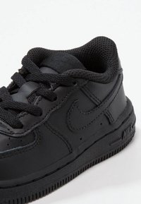 Svart lädersneaker med texturerad meshfoder, platta svarta snörningar och en tjock gummisula. Har Nike-logotypen präglad på sidan.