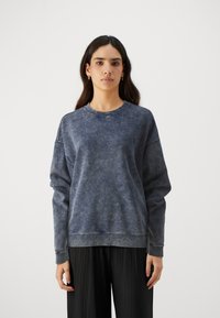 Mørkeblå sweatshirt i et blødt, teksturert stoff med rund hals og senkede skuldre. Har et subtilt logo på forsiden.