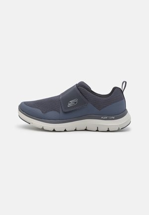 Zapatillas slip-on de color azul marino con tejido texturizado y acentos lisos. Presentan una suela blanca flexible con la etiqueta "FLEX-LITE."