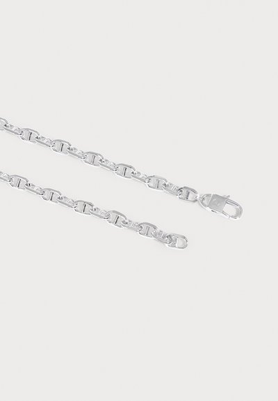 Collier chaîne en argent avec des maillons ovales et un fermoir mousqueton sur un fond clair uni.