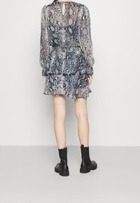 Krátké šaty s modro-beige hadím vzorem. Mají dlouhé rukávy, peplum lem a otevření ve tvaru klíče na zadní straně. Nosené s černými botami do kotníku.