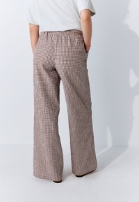 Rudos ir baltos spalvos languotos plačios kelnės su elastinga juosmens juosta ir šoninėmis kišenėmis. Audinys atrodo lengvas ir sklandžios tekstūros.