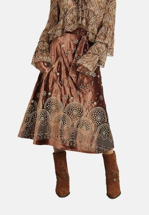 Falda de terciopelo marrón con intrincados patrones de lentejuelas doradas y plateadas, combinada con una blusa estampada y botines de ante marrones.