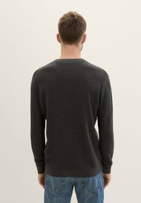 Suéter de punto gris oscuro con cuello redondo, mangas largas y puños de canalé. Combinado con jeans de mezclilla azules, que muestran un acabado texturizado.