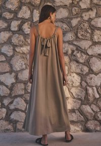 Robe longue vert olive à coupe décontractée, avec un dos froncé et un détail de nœud. Le tissu semble lisse et léger.