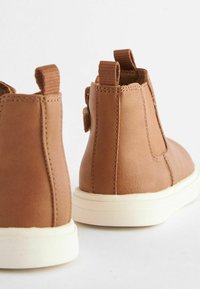 Brune læder ankelstøvler med elastiske sidepaneler og pull tabs, featuring en hvid gummisål og glat tekstur. Set fra bagpå.