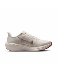 Ανοιχτό μπεζ παπούτσι τρεξίματος Nike με μεταλλικό λογότυπο Swoosh, παχιά μαλακή σόλα και κόκκινες λεπτομέρειες στην εξωτερική σόλα, εμφανιζόμενο σε πλάγια όψη.