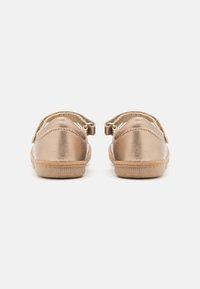 Zapatos metálicos dorados de forma redondeada, con una tira de velcro y una suela texturizada beige. Acabado suave con detalles de costura mínimos.