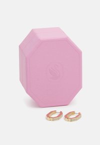 Ružová osemhranná šperkovnica s texturovaným povrchom, vo vnútri obsahuje zlaté kruhové náušnice ozdobené priehľadnými kryštálmi na jednej strane.