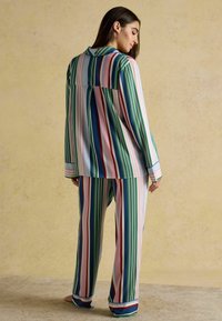 Striped pajama set in blue, green, red, and pink. The shirt has a collar and long sleeves; the pants are loose-fitting with cuffs. Soft fabric texture.