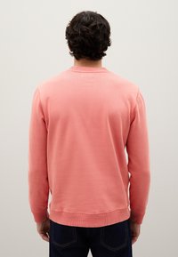 Sudadera de cuello redondo en rosa claro con puños y dobladillo acanalados. Tejido suave, corte relajado. La vista trasera muestra una textura lisa y sin patrones visibles.