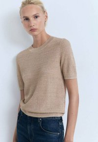 Strik bluse med korte ærmer i beige, med et struktureret mønster og rund halsudskæring, parret med mørkeblå jeans.