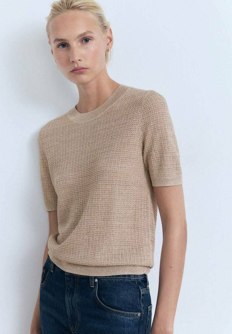 Strik bluse med korte ærmer i beige, med et struktureret mønster og rund halsudskæring, parret med mørkeblå jeans.