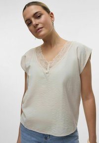 Top beige chiaro con scollatura a V e bordi in pizzo, con maniche corte, un tessuto leggermente texture e un fit rilassato.