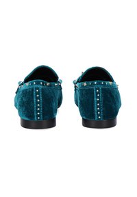 Zapatillas de terciopelo verde azulado con acentos de tachuelas y una superficie texturizada, que cuentan con una suela plana negra y remaches decorativos a lo largo de la parte trasera.