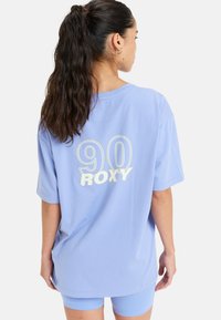 Jasnoniebieska, oversize koszulka z miękkiej bawełny. Na plecach widnieją duże napisy "90" oraz "ROXY" w kontrastującym białym kolorze. Krótkie rękawy.