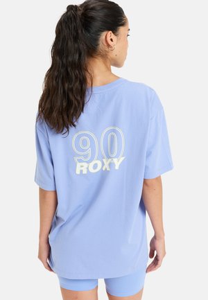 T-shirt surdimensionné bleu clair en coton doux. Présente un grand "90" et "ROXY" imprimés au dos en blanc contrasté. Manches courtes.