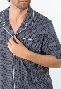 Chemise de pyjama à manches courtes couleur marine, ornée d'un motif à pois blancs, avec un passepoil contrasté le long du col et une poche poitrine.
