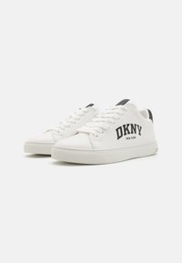 Bijele tenisice od glatke kože s zaobljenim vrhom, crnim akcentima na peti i natpisom "DKNY NEW YORK" otisnutim podebljano sa strane.