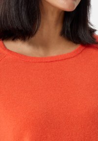 Maglione arancione brillante con una texture liscia e morbida e un collo ampio e arrotondato. Il tessuto sembra leggero e leggermente aderente.