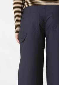 Pantaloni a gamba larga blu navy con due tasche posteriori e un tessuto texture. Una maglietta a righe a maniche lunghe parzialmente visibile di lato.