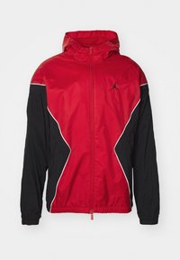 Červeno-černá bunda na zip s kapucí, zdobená bílými akcenty a logem. Vyrobená z lehkého materiálu, má mírně přiléhavý střih.