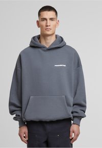 Grijze hoodie met lange mouwen, een front pocket en de tekst "PROHIBITED" in wit. Zachte textuur en een relaxte pasvorm.