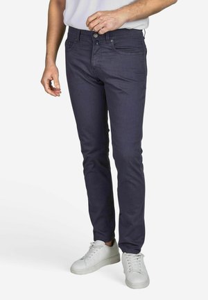 Marineblauwe slim-fit jeans van een katoenmix, met vijf zakken, een ritsopening en subtiele stikseldetails. Draagt met witte sneakers.