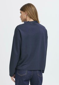Marinblå sweatshirt med hög krage, sänkta axlar och en avslappnad passform. Mjuk textur, inga synliga mönster eller metall detaljer.